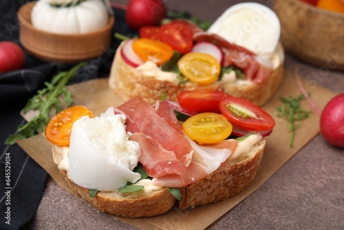 Delicious sandwiches with burrata cheese, ham, radish and tomatoes on brown textured table, closeup