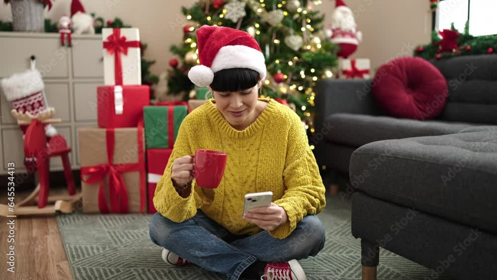 Young chinese woman using smartphone drinking coffee by christmas tree at home Young chinese woman using smartphone drinking coffee by christmas tree at home