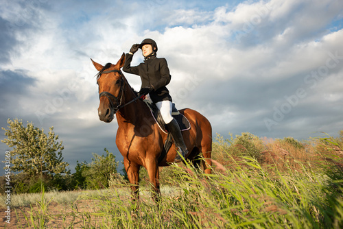 Horsewoman in equestrian sports gear, riding a horse, against an expressive sky, horseback riding in the open air