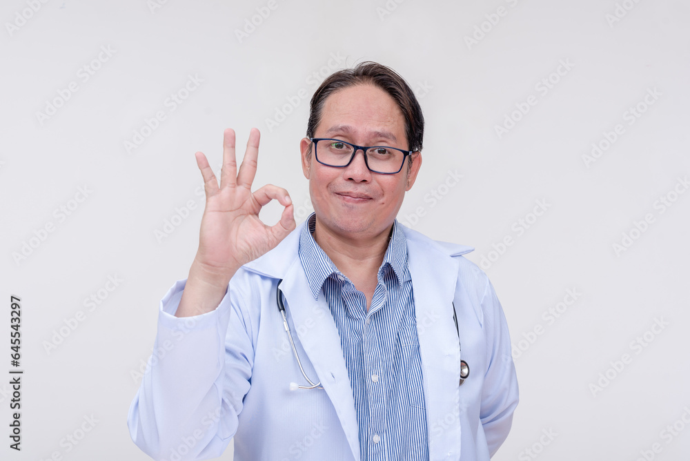A supportive family doctor makes a reassuring gesture, making the ok sign. Giving his approval. Of asian descent, middle aged male in his 40s. Isolated on a white background. A supportive family doctor makes a reassuring gesture, making the ok sign. Giving his approval. Of asian descent, middle aged male in his 40s. Isolated on a white background.