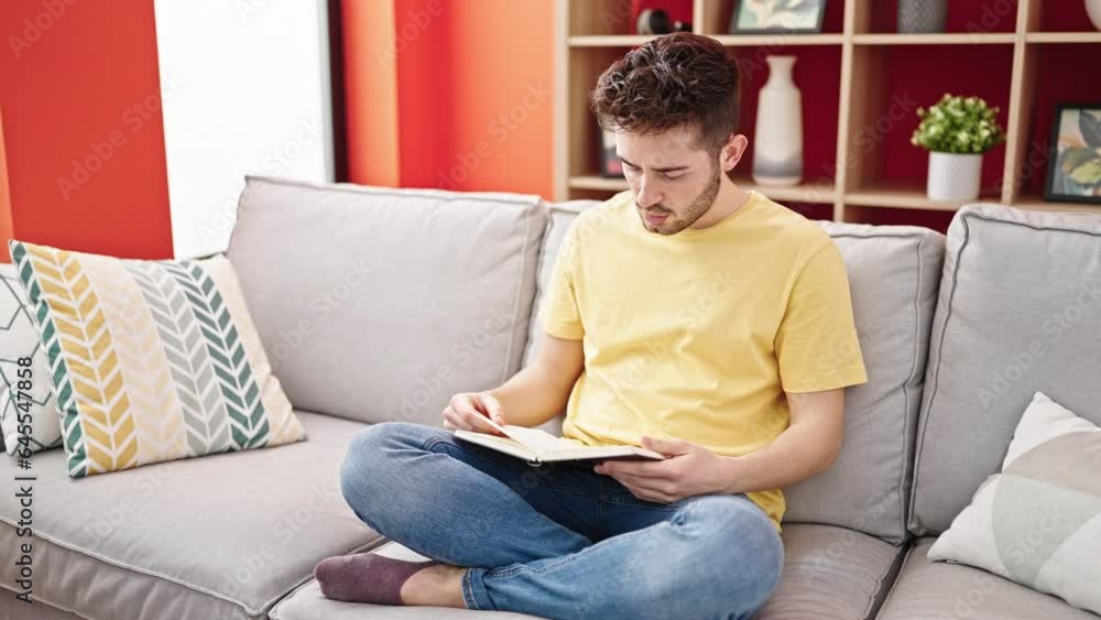 Young hispanic man reading book sitting on sofa at home Young hispanic man reading book sitting on sofa at home