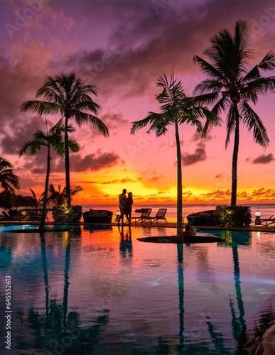 Fototapeta Naklejka Na Ścianę i Meble -  a couple of men and women watching the sunset on a tropical beach in Mauritius with palm trees by the swimming pool, Tropical sunset on the beach in Mauritius.