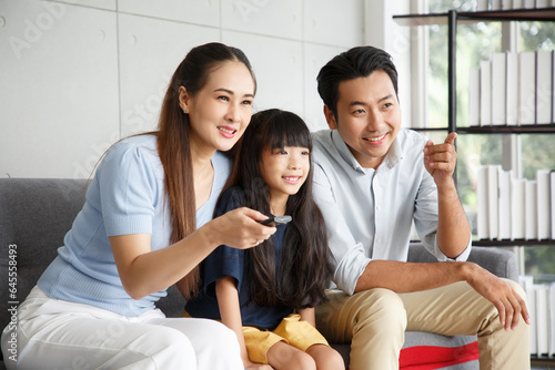 Happy Asian family lifestyle enjoy watching TV in living room at home. Happy Asian family portrait with mother, father and daughter