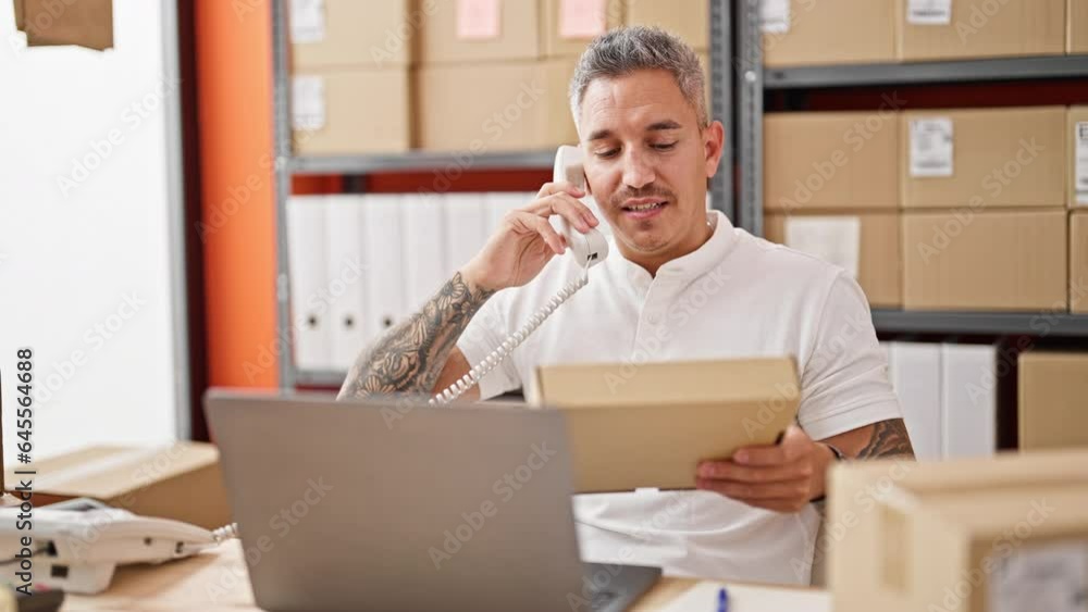 Young hispanic man ecommerce business worker talking on telephone holding package at office Young hispanic man ecommerce business worker talking on telephone holding package at office