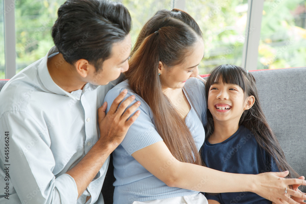 Portrait of a happy young family. Mom, dad and daughter look at the camera and smile sitting on sofa in living room. The faces of Asian parents and their child. Portrait of a happy young family. Mom, dad and daughter look at the camera and smile sitting on sofa in living room. The faces of Asian parents and their child.