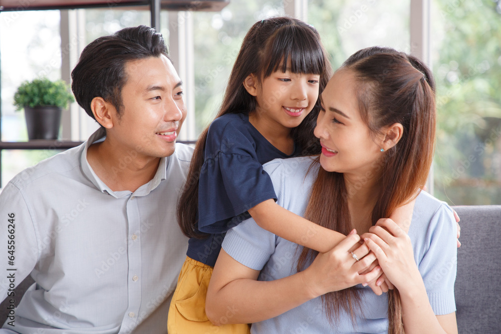 Portrait of a happy young family. Mom, dad and daughter look at the camera and smile sitting on sofa in living room. The faces of Asian parents and their child. Portrait of a happy young family. Mom, dad and daughter look at the camera and smile sitting on sofa in living room. The faces of Asian parents and their child.