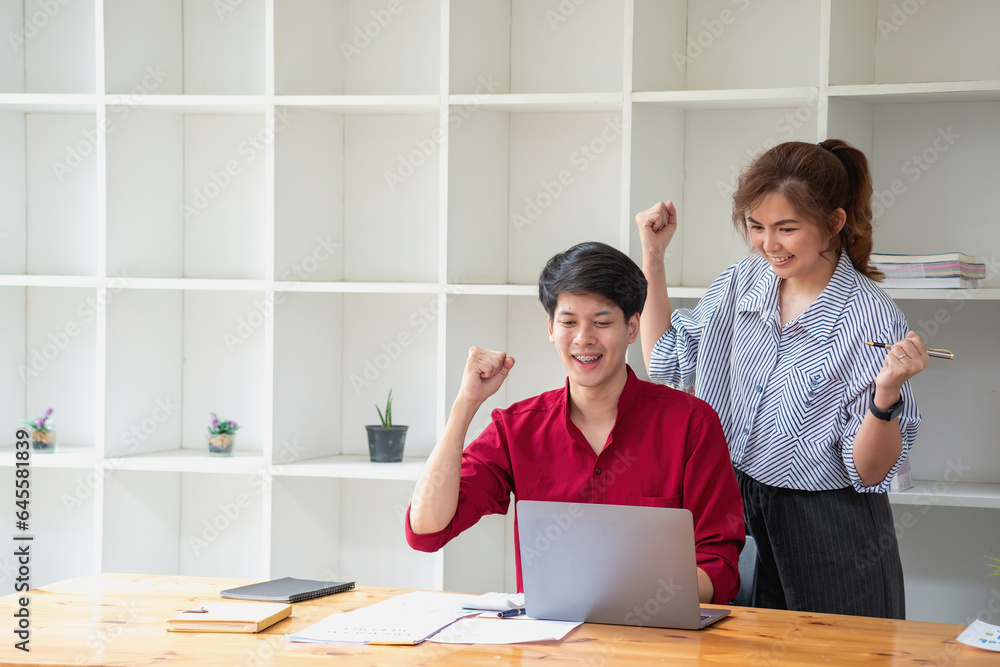 Cheerful business people using a laptop in an office. Happy young entrepreneurs smiling while working together in a modern workspace. Two young business people are sitting together at a table. Cheerful business people using a laptop in an office. Happy young entrepreneurs smiling while working together in a modern workspace. Two young business people are sitting together at a table.