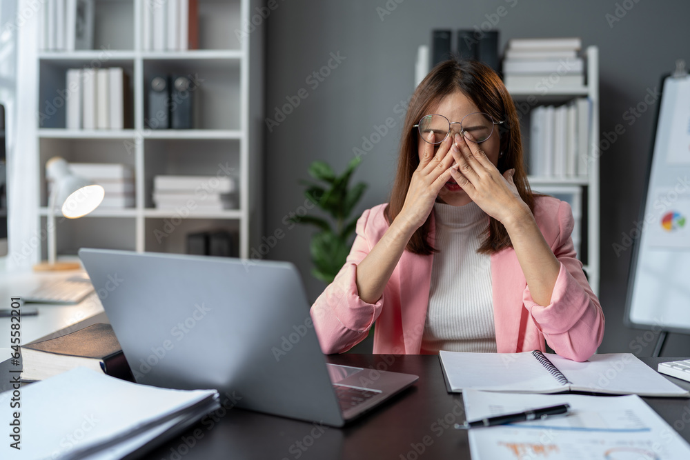 Stressed, tired, sleepy businesswoman bored from sitting at a desk for long hours and having office syndrome while working with laptop and financial paperwork. office marketing. Stressed, tired, sleepy businesswoman bored from sitting at a desk for long hours and having office syndrome while working with laptop and financial paperwork. office marketing.