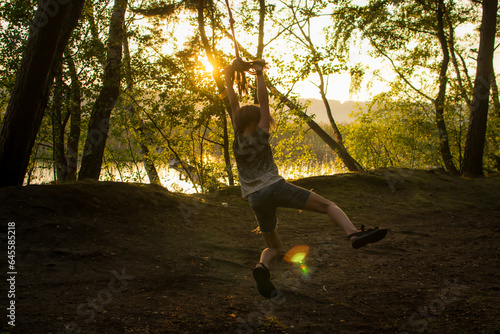 A young guy, a teenage boy, rides a bungee, on a rope in a forest among birches on the lake.