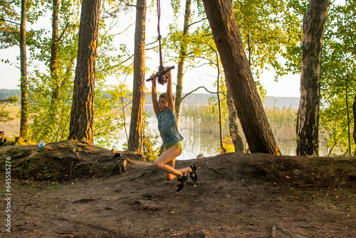 A young guy, a teenage boy, rides a bungee, on a rope in a forest among birches on the lake.
