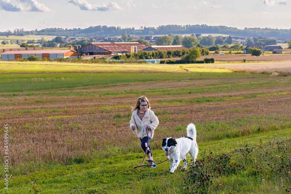 Obraz premium Little preschool girl walking with her dog. Cute kid and family pet in nature, fields and forest in late summer. Love and friendship between child and dog. Having fun together.