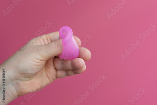 Reusable menstrual cup in the hands of a woman on a delicate pink background. How to fold the menstrual cup. Сoncept female intimate hygiene period products and zero waste. Minimalism. Copyspace.