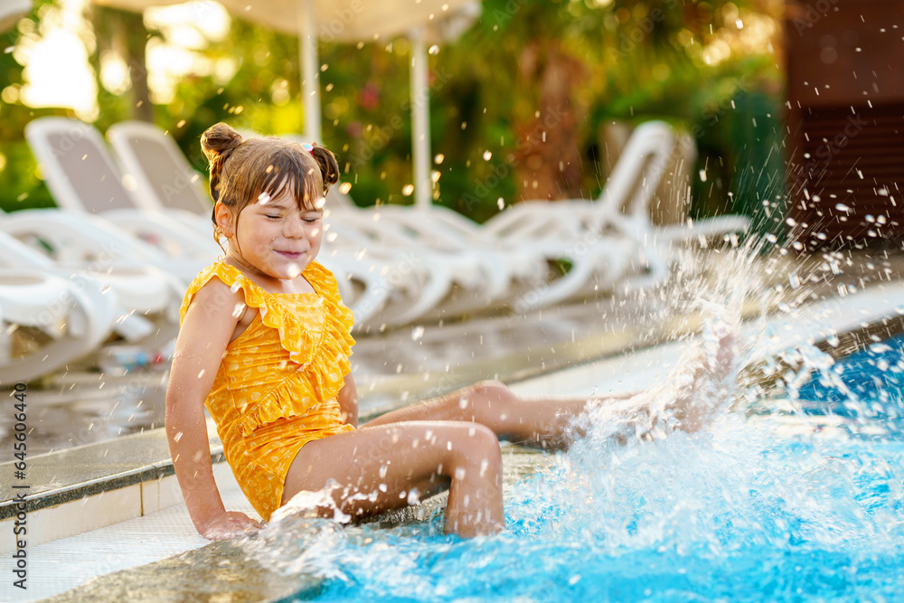 Little preschool girl playing in outdoor swimming pool by sunset. Child learning to swim in outdoor pool, splashing with water, laughing having fun. Family vacations. Healthy children sport activity Little preschool girl playing in outdoor swimming pool by sunset. Child learning to swim in outdoor pool, splashing with water, laughing having fun. Family vacations. Healthy children sport activity