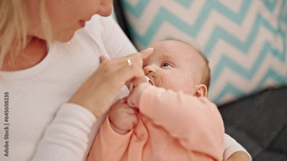 Mother and daughter sitting on sofa sucking pacifier touching nose at home