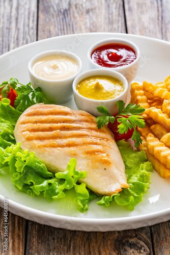 Grilled chicken breast, French fries and fresh vegetables on wooden table 