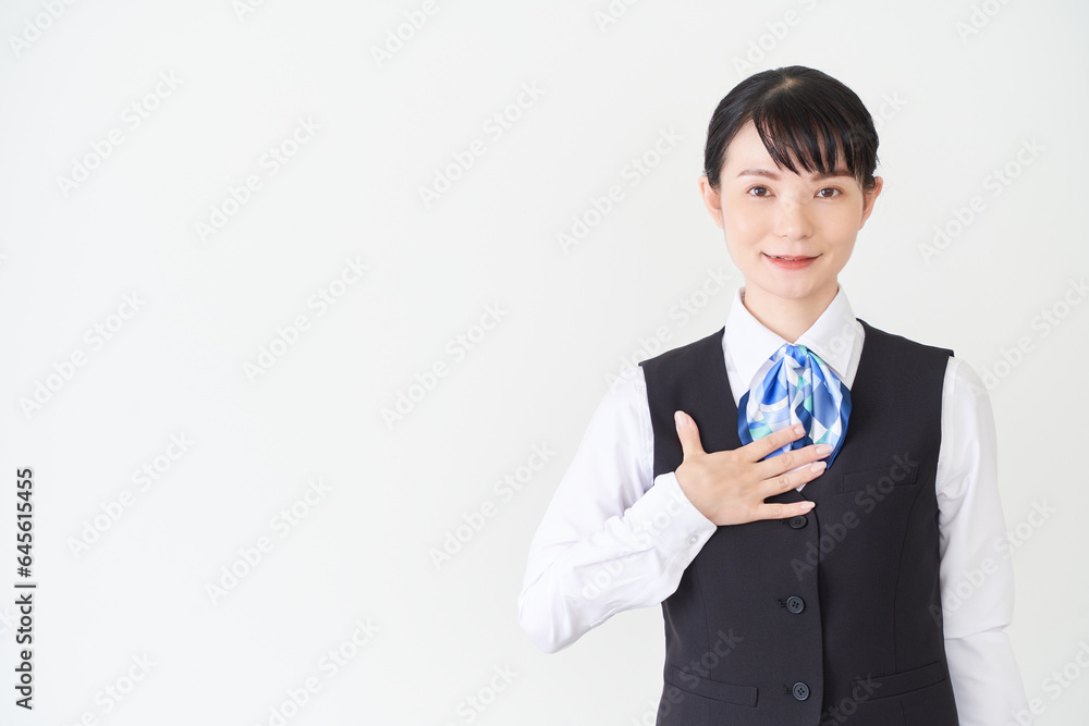 胸に手を当てるベストにリボンタイの制服を着た、受付業務、事務業務の女性
