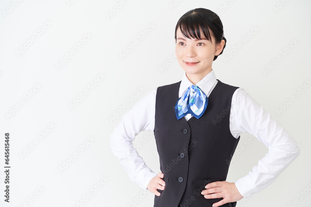 腰に手を当てるベストにリボンタイの制服を着た、受付業務、事務業務の女性