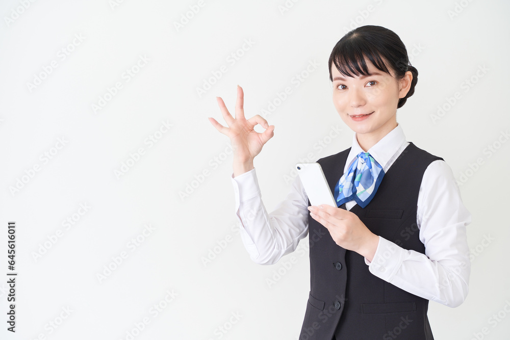 スマートフォンを操作するベストにリボンタイの制服を着た、受付業務、事務業務の女性