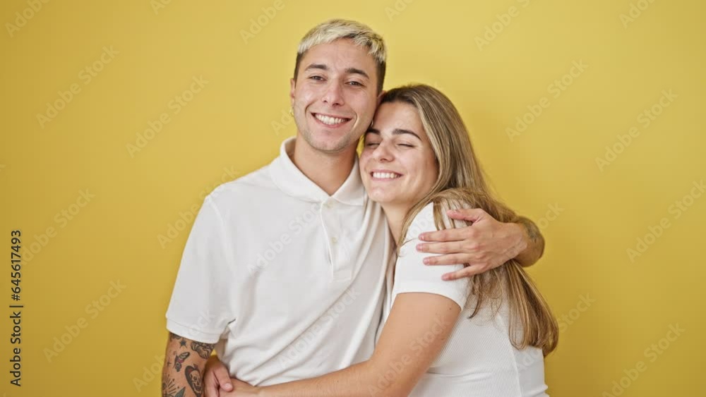 Beautiful couple smiling confident hugging each other over isolated yellow background Beautiful couple smiling confident hugging each other over isolated yellow background