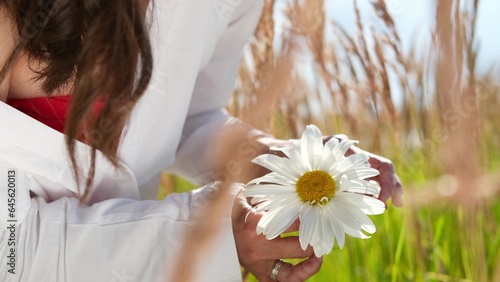 Happy woman with big chamomile in her hand in summer field. Carefree girl enjoys freedom and tranquility in the countryside during her vacation. The concept of rest or relaxation and happiness or photo