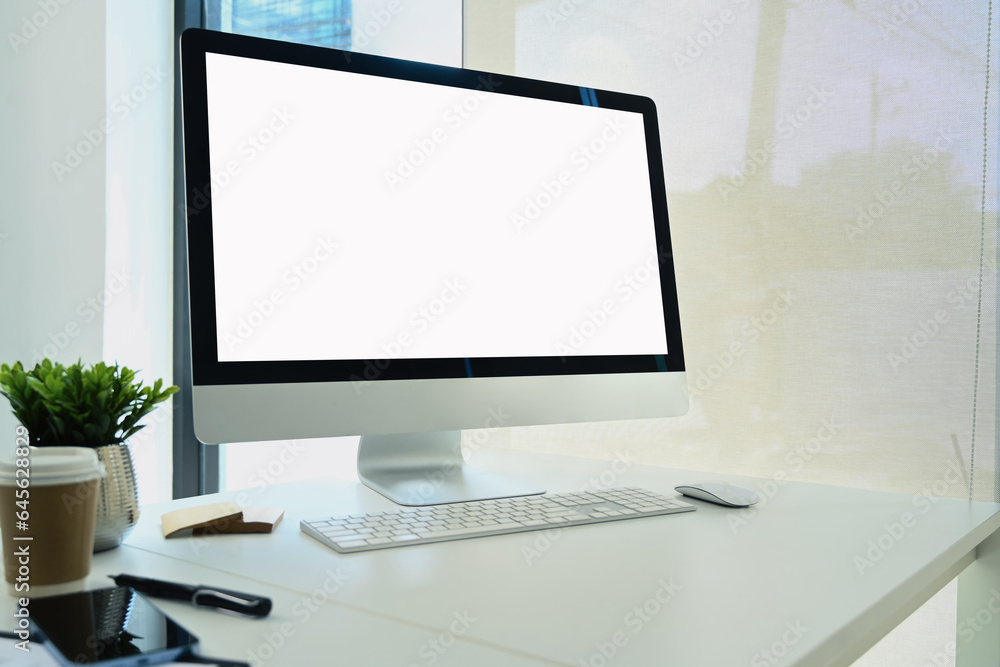 Fototapeta premium Comfortable workplace with blank screen computer monitor, paper cup, smartphone and potted plant on white table