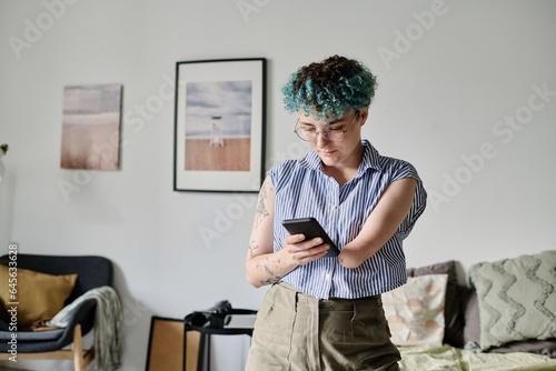Young woman reading message on her smartphone while standing in the living room photo