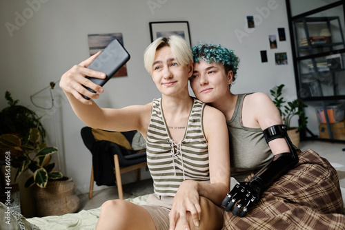 Young lesbian couple making selfie portrait on smartphone while sitting in the room