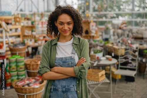 Slika na platnu Smiling female garden shop seller standing on flower store background