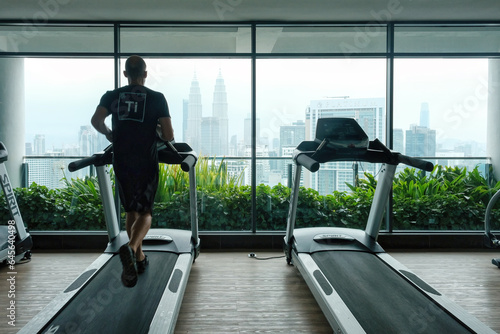 Canvas Print A man runs on a treadmill looking at the city and Petronas Twin Towers
