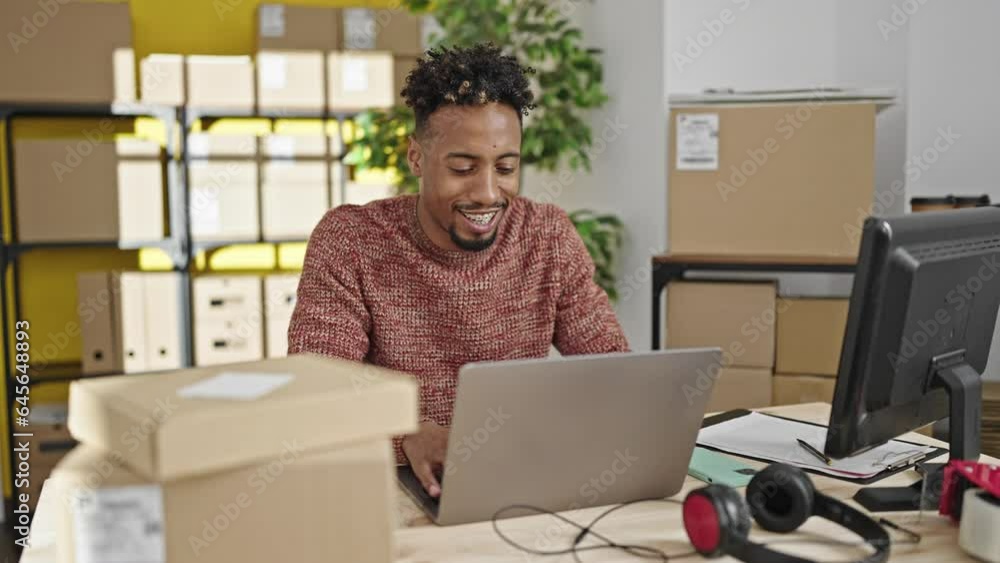 African american man ecommerce business worker using laptop sitting on table at office African american man ecommerce business worker using laptop sitting on table at office