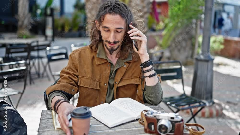 Young hispanic man tourist talking on smartphone sitting on table taking notes at coffee shop terrace Young hispanic man tourist talking on smartphone sitting on table taking notes at coffee shop terrace