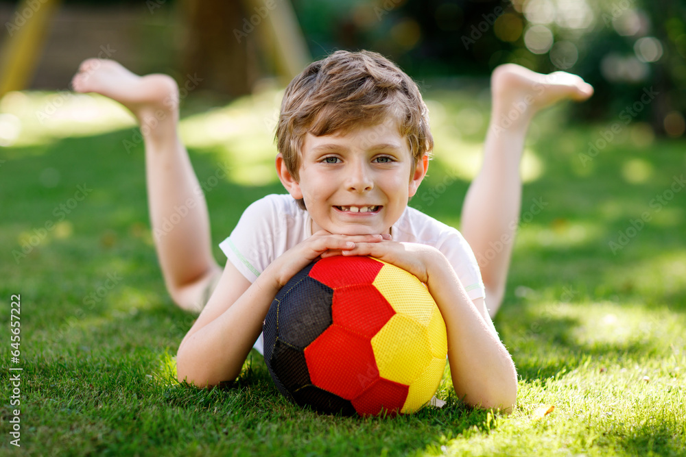 Obraz premium Happy active kid boy playing soccer with ball in German flag colors. Healthy child having fun with football game and action outdoors