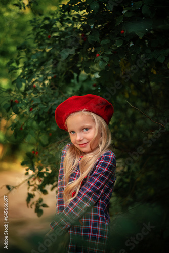 Portrait of a blonde little girl in a red beret and a plaid dress