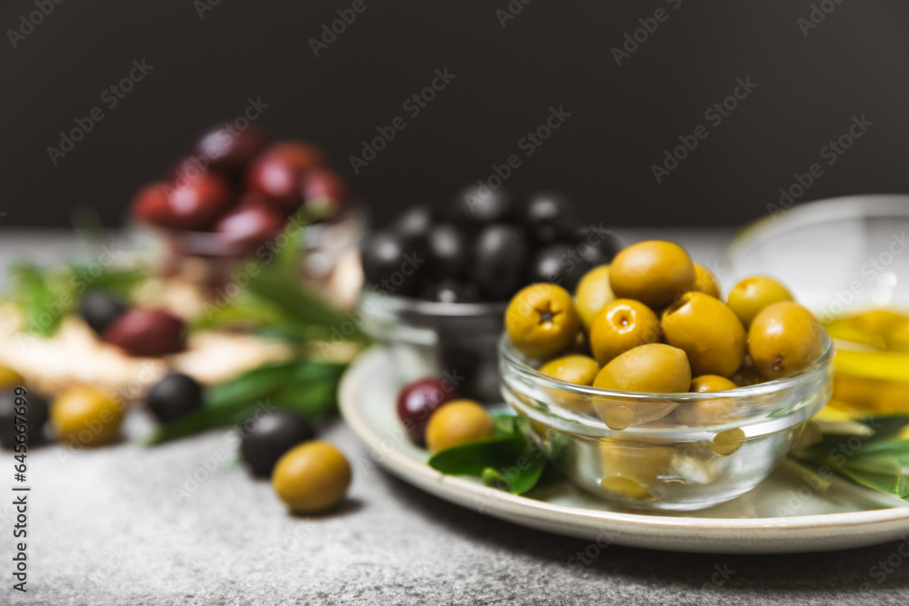 A set of green, red and black olives on a marble background. Various types of olives in bowls and fresh olive leaves. Vegan. Olive fruits. Place for text. Copy space.