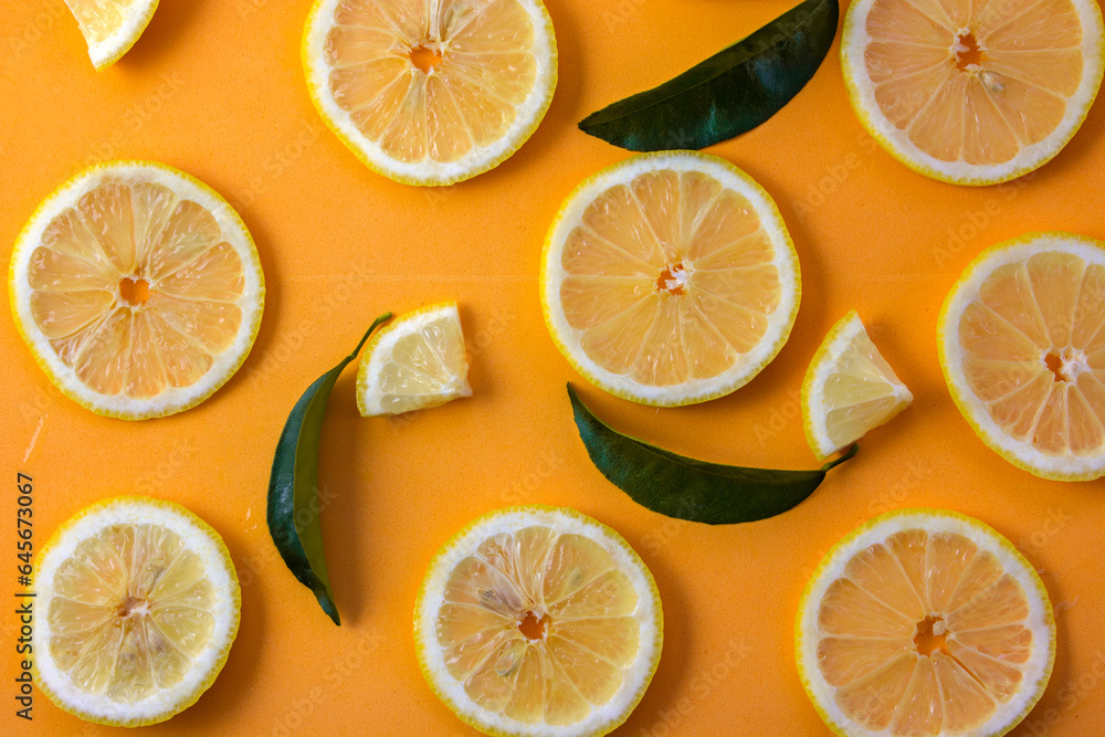 Obraz premium Lemon slices adorned with green leaves on an orange background offer a vivid and tropical display