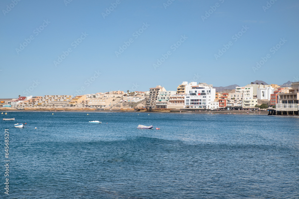 View from across the pier of the little picturesque town, perfect summer vacation destination for tourists interested in doing watersports, El Medano, Tenerife, Canary Islands, Spain