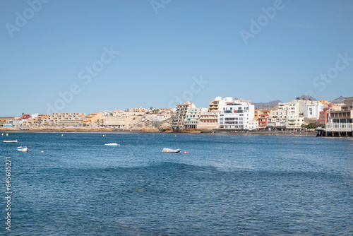 Fototapeta Naklejka Na Ścianę i Meble -  View from across the pier of the little picturesque town, perfect summer vacation destination for tourists interested in doing watersports, El Medano, Tenerife, Canary Islands, Spain