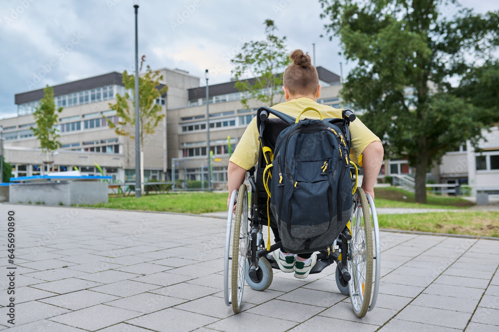 Obraz premium Back view, child preteen boy on wheelchair going to school building