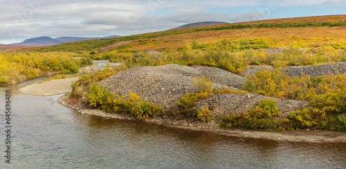 Tundra landscape in Western Alaska with rolling hills piles of mine tailings left behind by a gold dredge and river in autumn colors in the vicinity of Nome, Alaska
