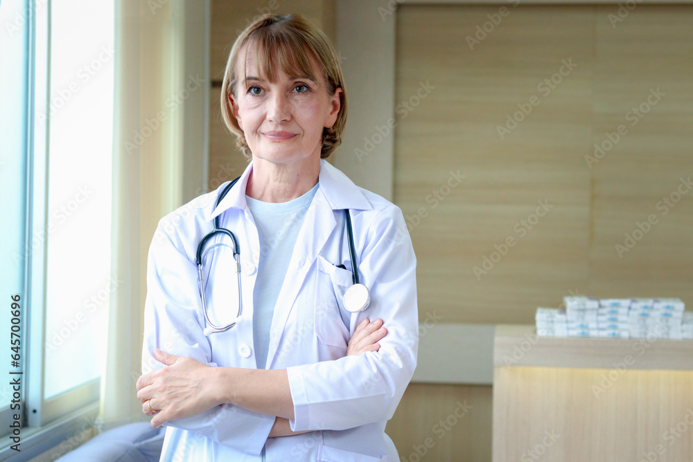 Portrait of smiling confident female doctor in white workwear with stethoscope, standing with arms crossed in clinic hospital. Professional senior woman doctor looking at camera at medical workplace. Portrait of smiling confident female doctor in white workwear with stethoscope, standing with arms crossed in clinic hospital. Professional senior woman doctor looking at camera at medical workplace.