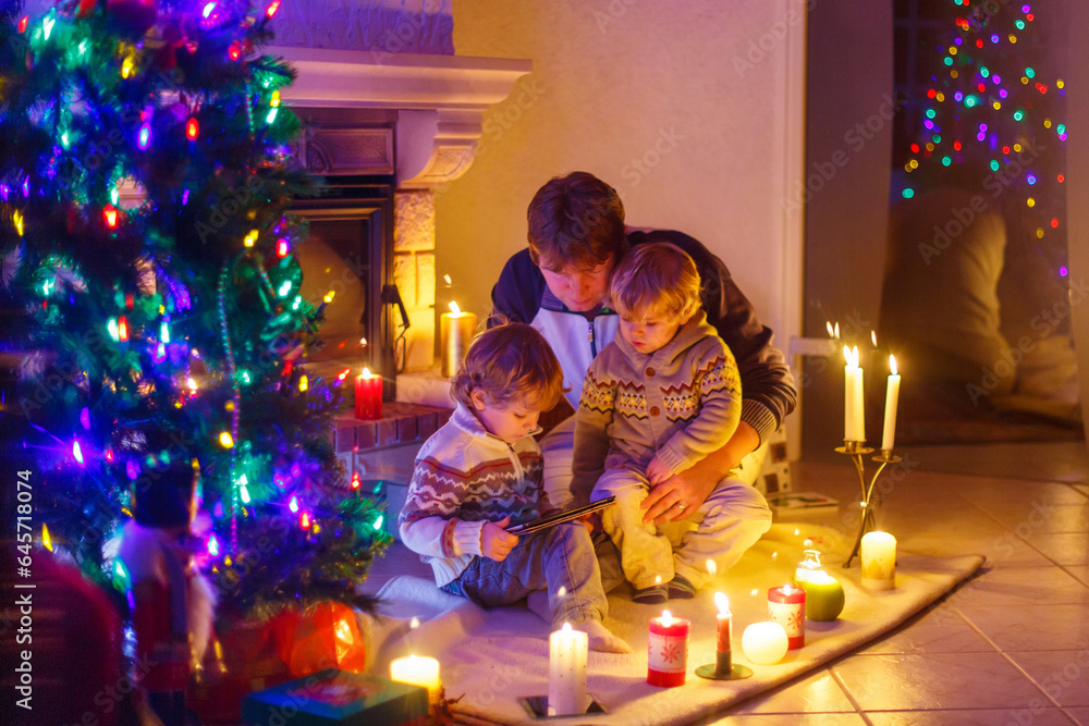 Father and his two little children sitting by fireplace chimney on Christmas Eve time.