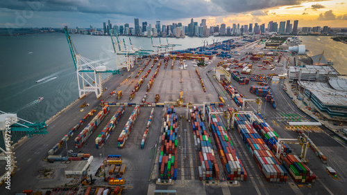 Aerial at sunset of Miami Downtown skyline with port and crane logistic container cargo boat 