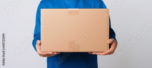 Young courier, the delivery man, holds an empty cardboard box isolated on a white background © chiew