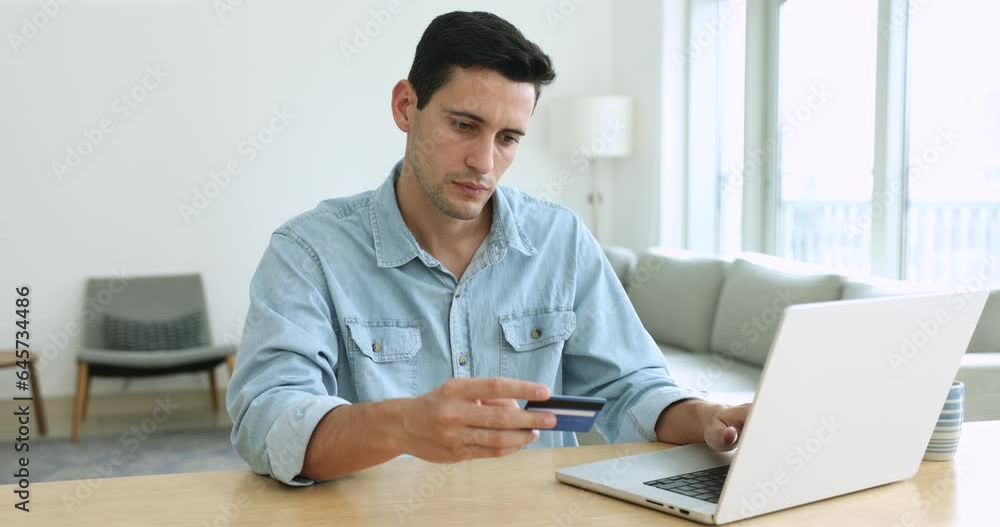 Millennial guy, satisfied shopper enters credit card data makes payment via on-line web store using laptop, pay bills, spending money on internet, getting cashback enjoy e-commerce e-shopping at home Millennial guy, satisfied shopper enters credit card data makes payment via on-line web store using laptop, pay bills, spending money on internet, getting cashback enjoy e-commerce e-shopping at home