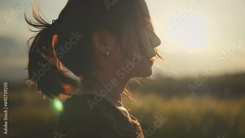 Close up portrait of Asian woman enjoying peaceful sunset. Wind blowing on hair, slow motion.
