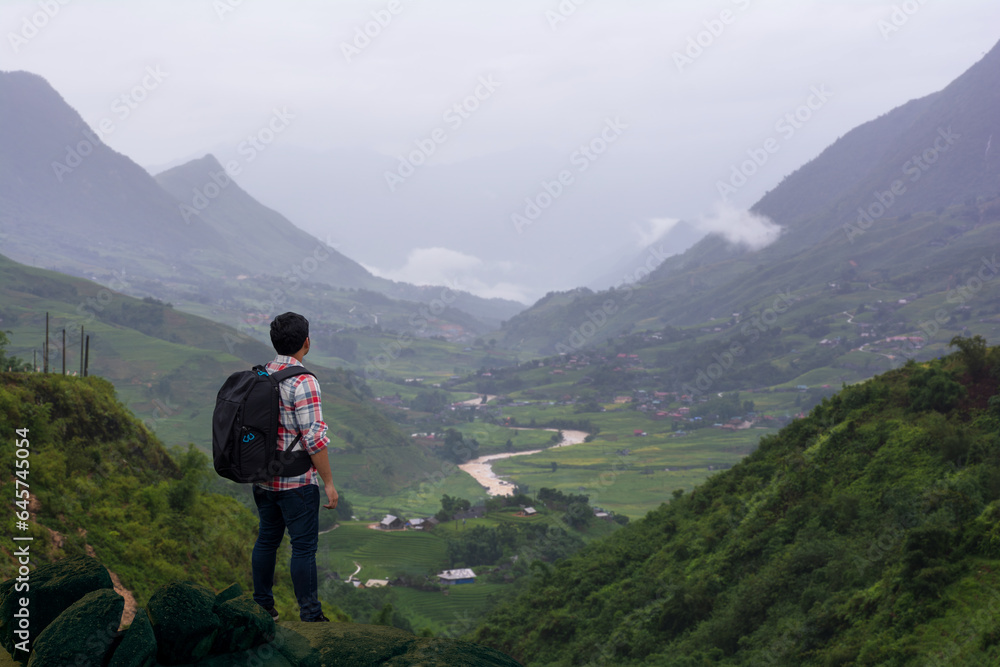 A young man was admiring the environment and watching the sunrise from a rock on top of a mountain.
