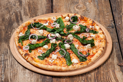 Studio shot of a hand made pizza with spinach, red onion slices and feta cheese on beautiful weathered wooden table
