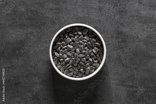 Sunflower seeds unpeeled in white bowl on dark background, top view, space to copy text