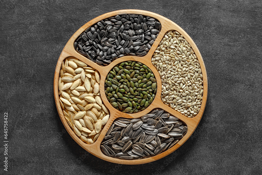 Sunflower and pumpkin seeds in a wooden round plate with cells, on dark background, top view