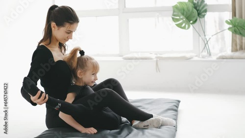 A gymnastics teacher helps young gymnastic girl stretching and do the splits